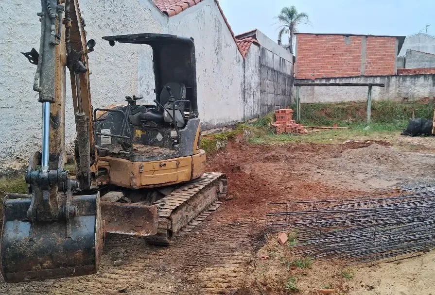 Mini escavadeira trabalhando em terreno residencial fechado por muros